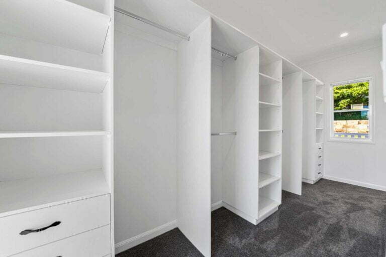 Large walk in wardrobe with in built shelving, clothes hanging racks and drawers. Natural lighting from the valley of Killarney spills in through a clear glass window.