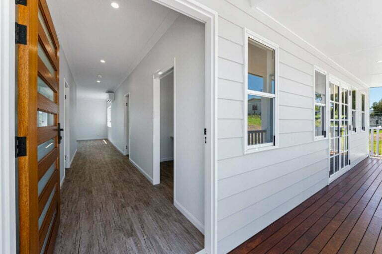 Front entry, set on a timber deck. External walls are clad in a neutral light grey linear board, the entry door way is extra wide with a feature timber door with natural stained finish for a welcoming and inviting entry for the family and friends
