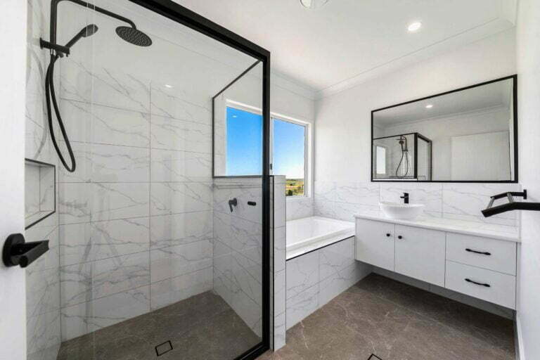 Large modern family bathroom featuring a large shower with built in storage, floor and wall tiles, neutral colour pallets with black fixtures, a single vanity unit and bathtub. Overall this is a very versatile family bathroom that makes great use of space.